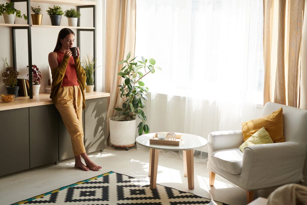 Woman in living room sipping tea in bright, decorated room.