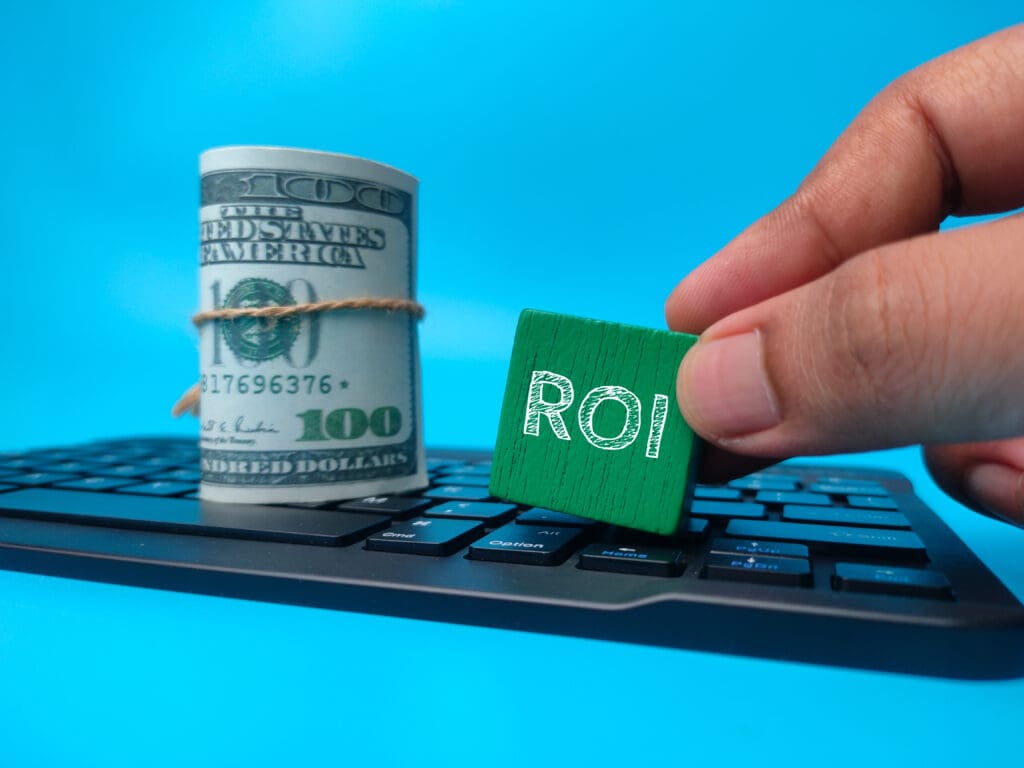 Hand holding colored block with word ROI on a blue background. 