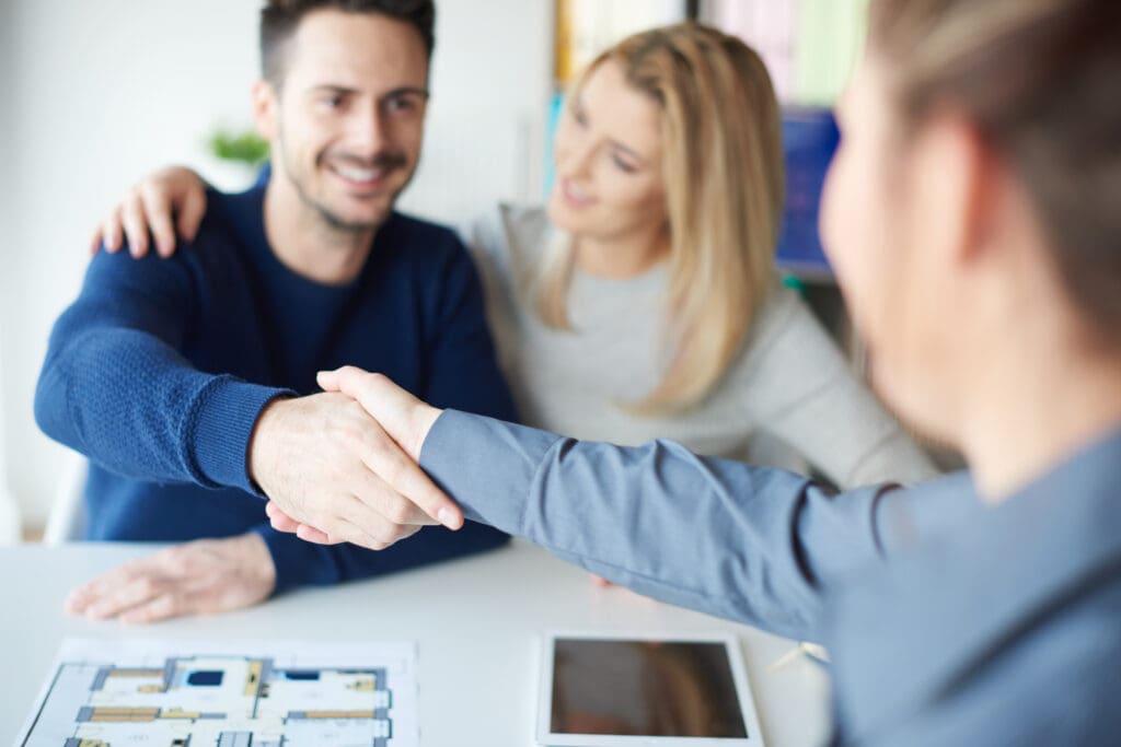 Real estate agent shaking hands with happy couple.  